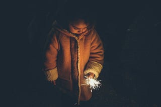 Child holding a sparkler in the darkness, her face lit by its glow