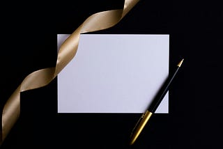 Blank Invitation, with a gold ribbon and a black, gold pen, on a black background.