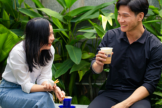 A guy together with a lady who is a yapper sitting on a bench enjoying their time together with coffee