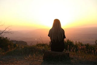 A woman sitting in front of a sunset