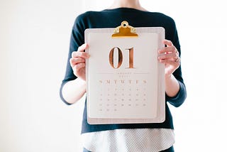 hands holding a clipboard with a month calendar on it and a big bold 01 in gold at the top of the paper on the clipboard
