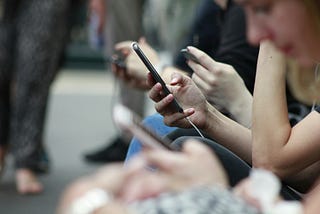 People sitting next to each other looking down at their smartphones.