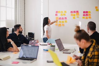 A standing woman discusses sticky notes on a wall with her seated colleagues