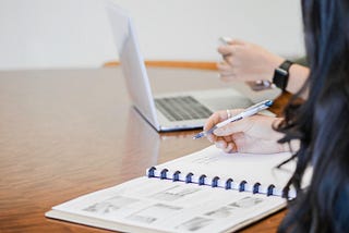 Planner open on a desk with a hand of a person holding a pen, as if they are about to write something down.