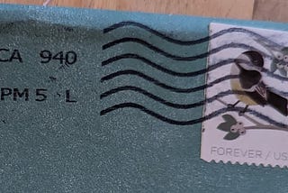 Books, Writing, and other Adventures: An image of the upper corner of a turquoise envelope, with a stamp obscured by black wavy postage marks.