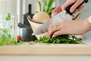 Someone is chopping up some green herbs on a wooden cutting board.