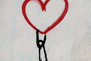 A figure drawn on a wall hangs beneath a heart, like a desperate man hanging from a balloon.