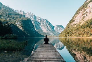A man sitting on the edge of a boating deck, looking out at the lake and mountains.