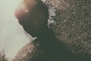 Two-tone, double-exposure, moody image of a person sillouetted in profile and water droplets and reflections