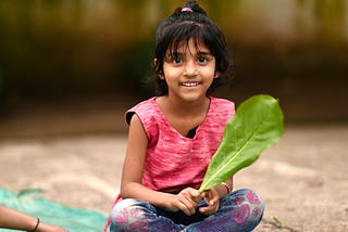 Little Indian girl sitting crosslegged holding a leaf