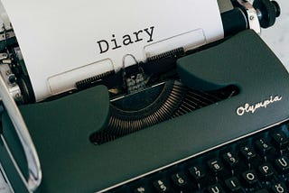 An antique typewriter with a blank page sitting on a writer’s desk.