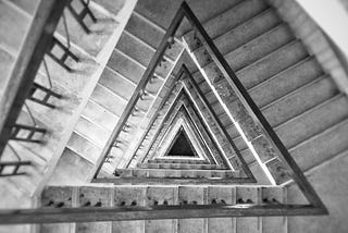 Black and white photo looking down a triangular spiral staircase.