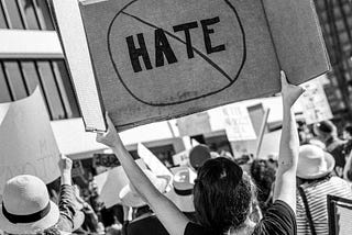 Protesting crowd with one woman holding cardboard sign that says “No hate”