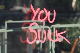 “You suck” written in red on glass