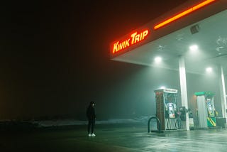 A person standing in the dark outside of a gas station.