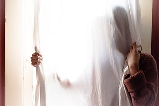 Woman mostly hidden behind white semi-transparent curtain