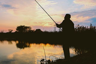 A man fishing at a lake at sunset or sunrise