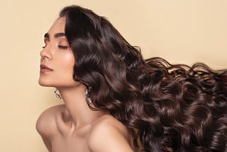 A brunettte woman with long wavy hair closes her eyes in a profile shot