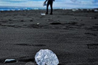 A single diamond on a black sand beach.