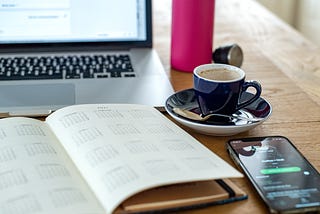 A laptop computer with a schedule, cup of coffee and cell phone on a desk