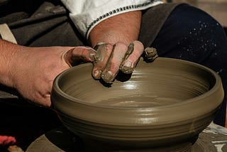 Male hands molding a pot on a potter’s wheel.