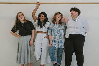 A picture of 4 smiling women of different body weight, height and color.