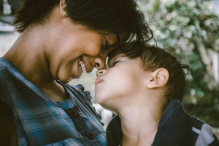 Mother and son, forehead to forehead. The mother is smiling and the son looks peaceful.