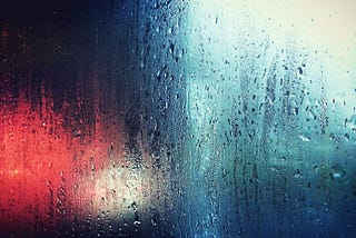 Image of a window in the rain. Colors are red and blue, but shapes are blurred.