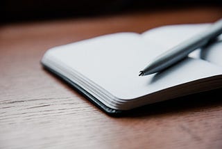 Picture of a desk with an open notebook and a pen.