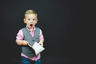 Young boy holding a book looks shocked at something he has read.