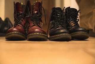 Two pairs of doc marten boots lined up next to each other, on the left a larger oxblood pair and on the right a smaller black pair