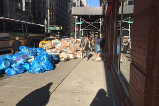 A sidewalk with New York City with a giant pile of clear trash bags taking up most of the sidewalk.