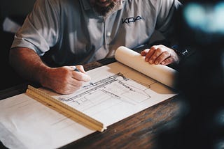 An architect at work sits at a wooden desk drawing a sketch.