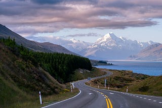Description from Klanarong Chitmung Peter’s Lookout, Ben Ohau, New Zealand photo is of a road with a mountain in the background, clear sky, and snow.