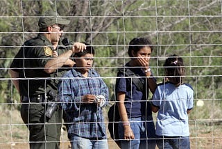 Migrant children and a Customs and Border Patrol (CBP) officer behind a fence
