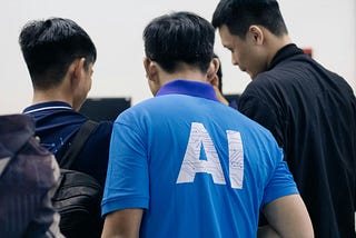 A group of men gather in a huddle. One of them wears a bright blue T-shirt with the letters AI on the back