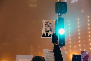 A person holding up a sign saying “Do not wait for leaders, become them”