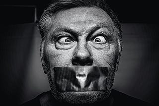 Censorship — A black and white image of an older man, eyes crossed, with duct tape over his mouth.