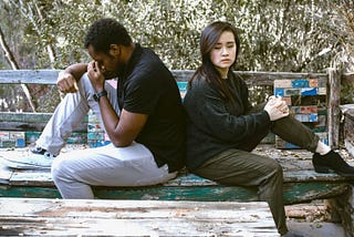 A couple sitting back to back on a bench.