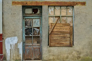 A photo of the front of a house, with a broken door and a broken window