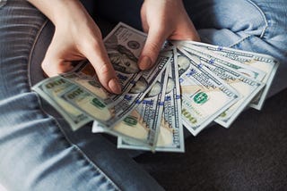 Hands hold a fan of $100 bills