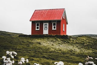 Little red cottage with a white door alone on a hill.