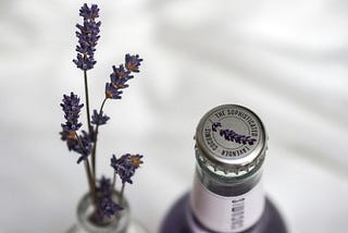 close-up on a couple sprigs of lavender coming out of a vase next to a bottled drink made with lavender