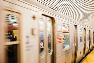 NYC subway rushing through the station. It’s slightly blurry closer to the camera.