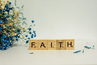 The word FAITH spelled out with Scrabble letter tiles.