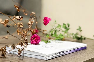 Two white volumes of poetry sitting on a desk, with dried flowers laid on top.