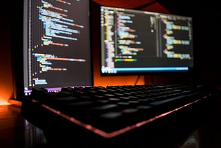 Two computer monitors displaying code in a dark room