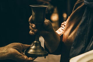 Cult member in a rope hands a glass of liquid to a follower