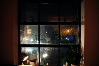 Empty, dark room, looking out through rain blurred glass onto a busy street at night