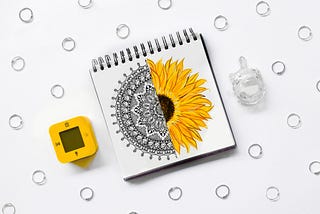 A picture of a sketchbook with a drawing of a half mandala and a half sunflower.